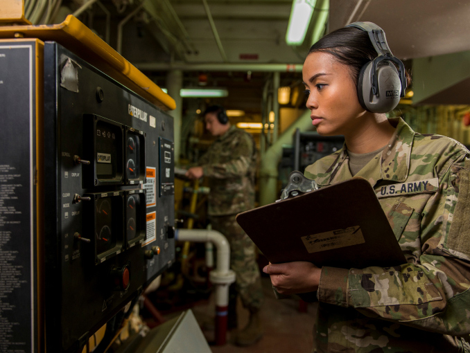 A female Soldier wearing headphones reading gauges on an Army watercraft