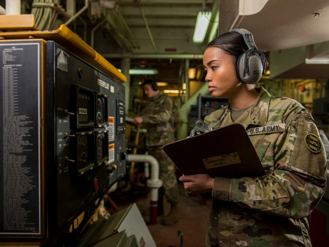 A female U.S. Army Reserve watercraft operator reading gauges in the control room of a military ship