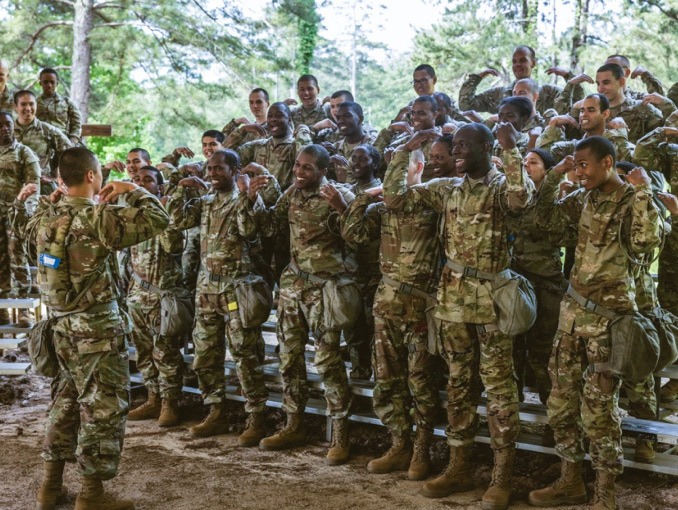 Un gran grupo de reclutas de Basic Training parados sobre vigas en un bosque