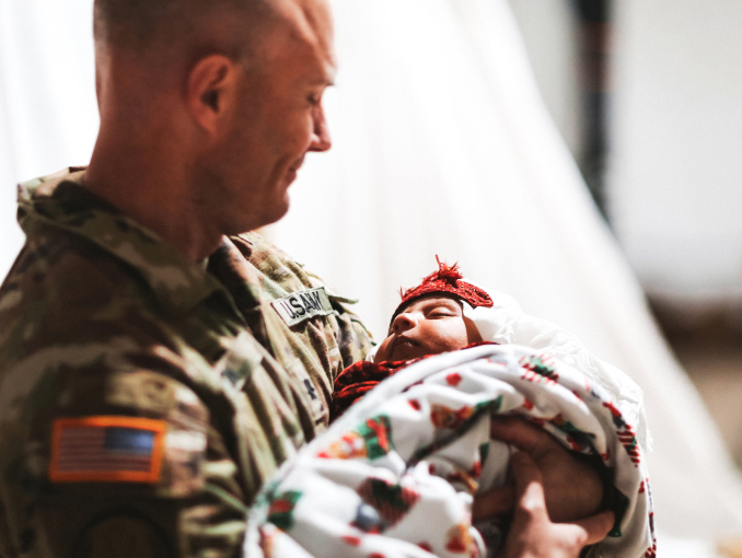 A male Soldier in combat uniform holding a newborn baby