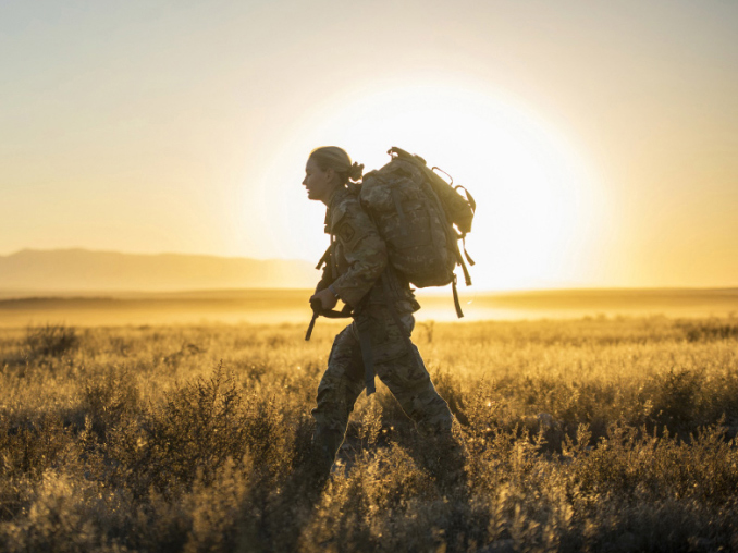 Una Soldado cargando una mochila en un campo durante el amanecer 