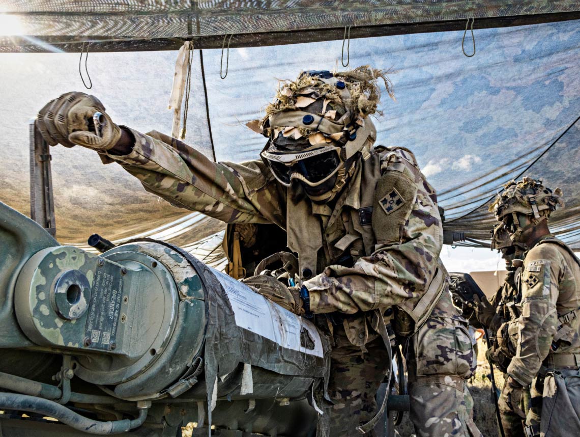 Soldier in full combat gear preparing field artillery equipment in an outdoor tent