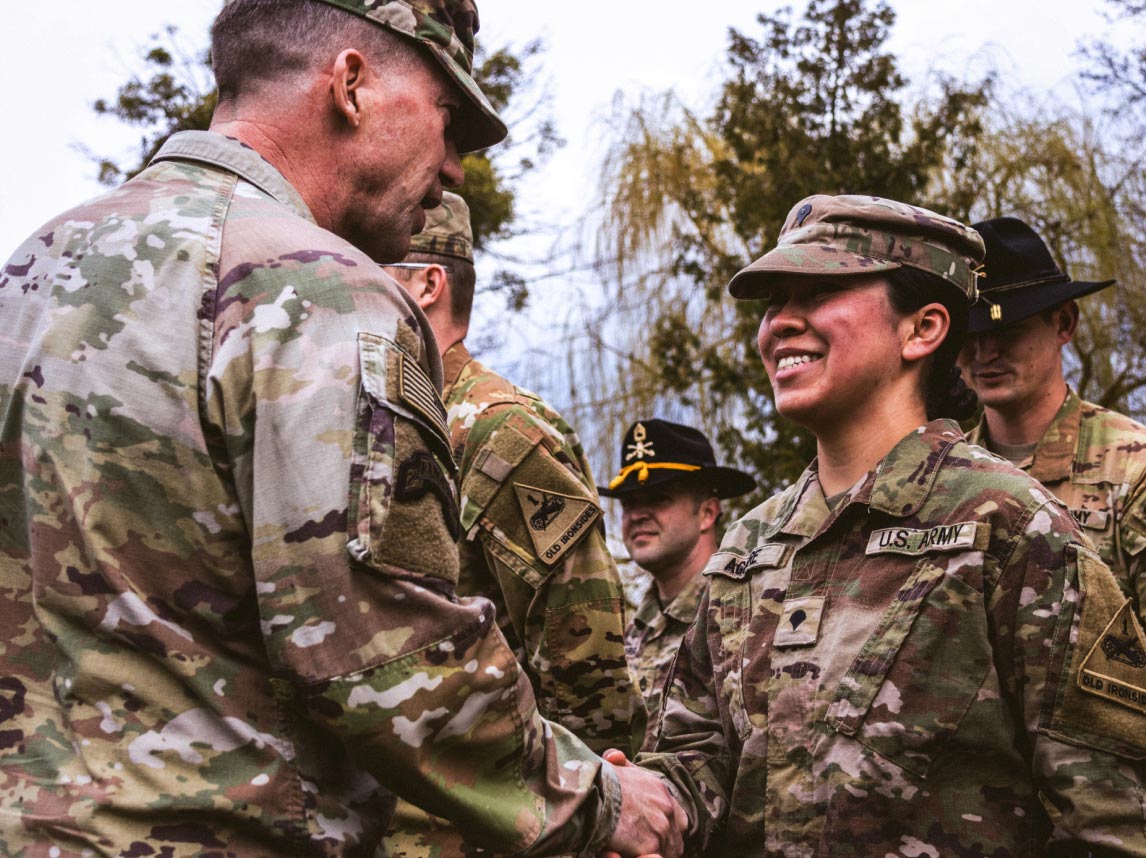 A smiling female Soldier shaking the hand of a male Soldier outdoors