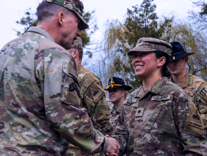 Una Soldado sonríe dándole la mano a un Soldado al aire libre