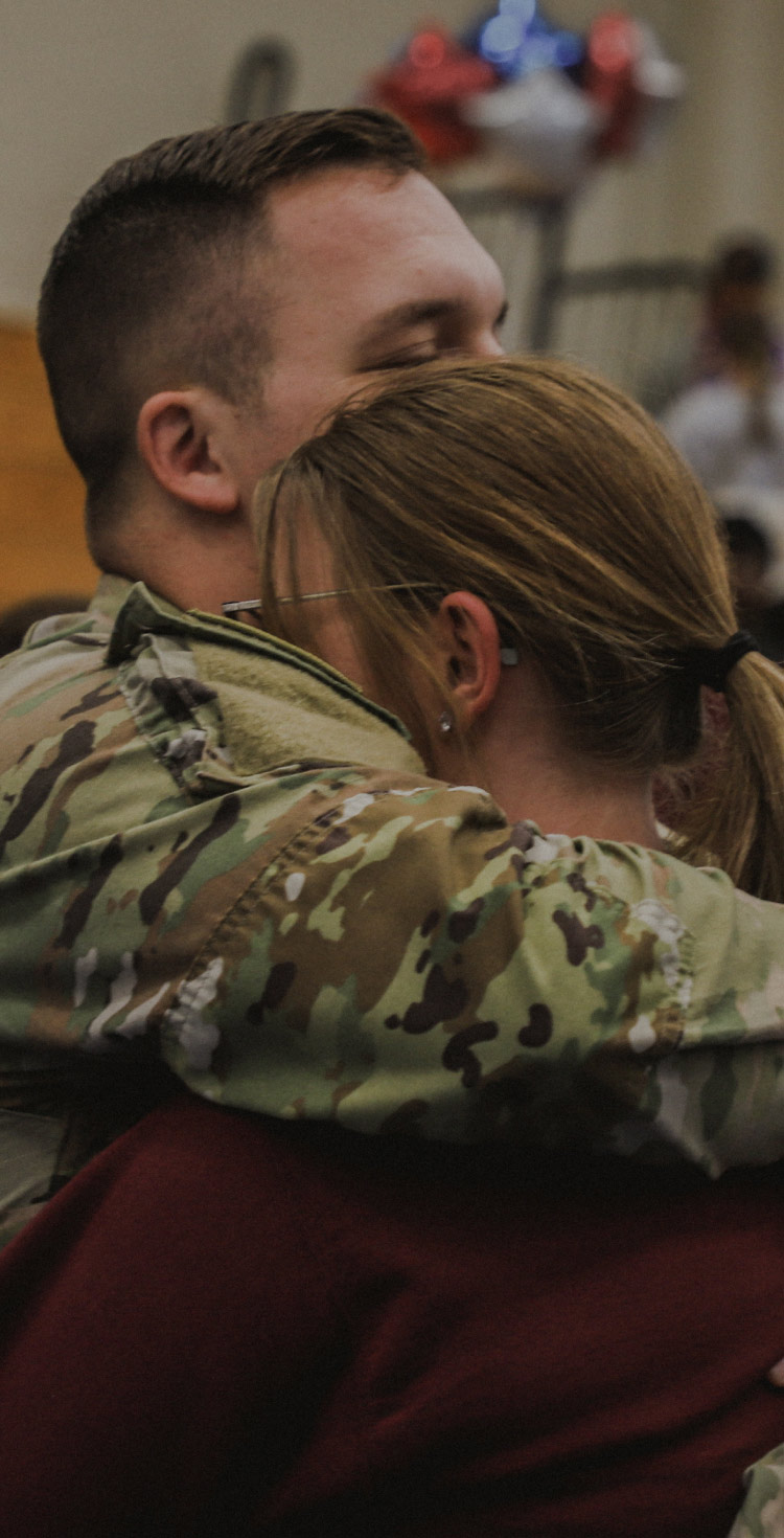 A male Soldier in combat uniform hugging his wife in a gymnasium