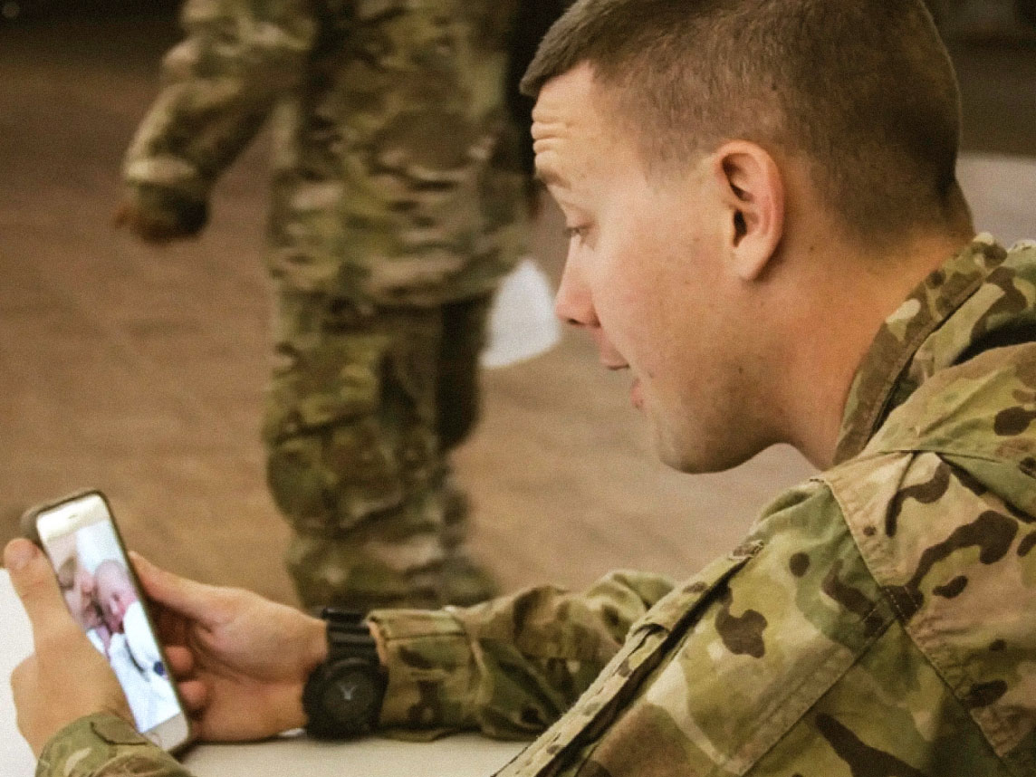 A Solider uses his phone to FaceTime with his wife and watch their new-born daughter