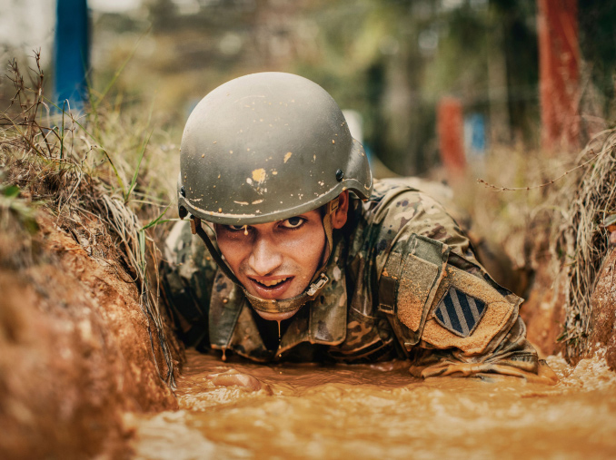 A male Soldier in combat uniform and hard helmet crawling through the mud