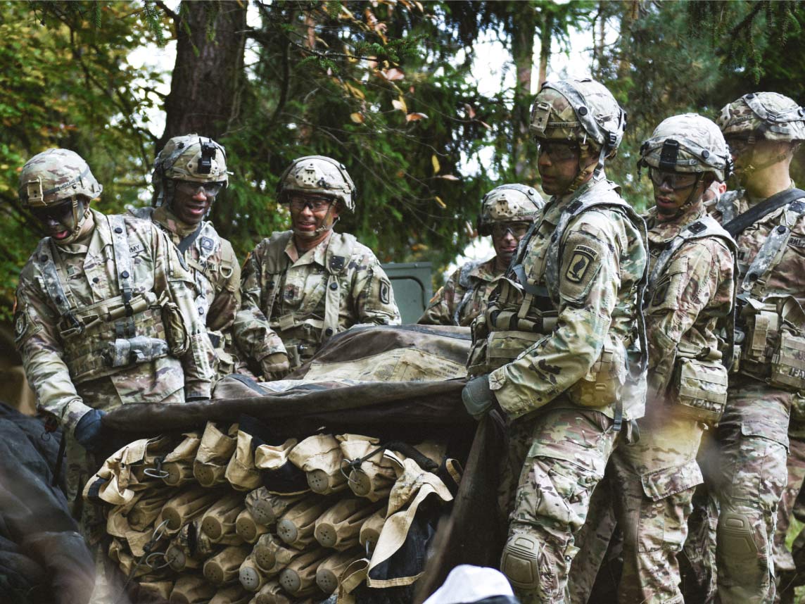 A group of seven Soldiers in combat uniform carrying a large tent in a bag