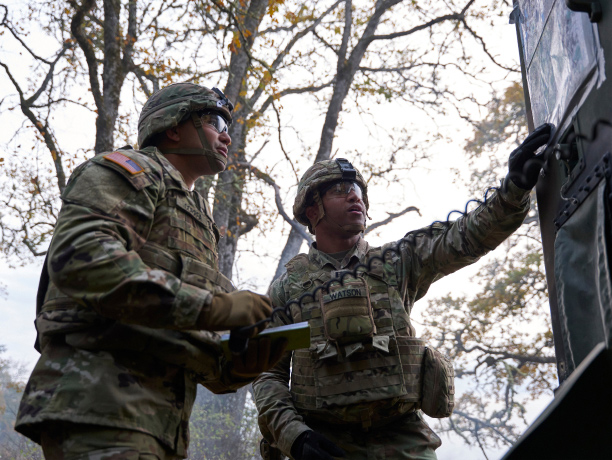 Two Soldiers in combat uniform looking at a bulletin board outdoors