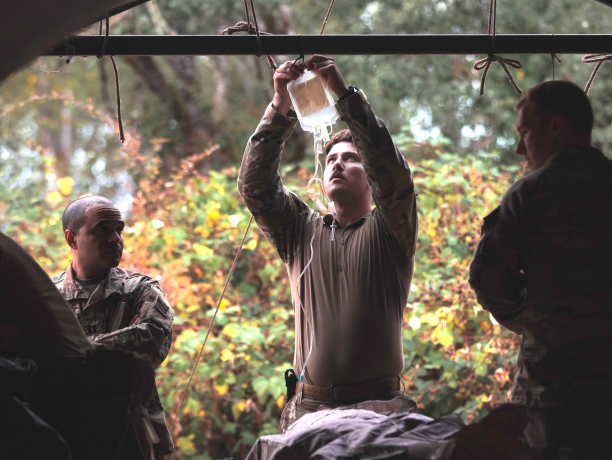 Un médico de combate del U.S Army cuelga una bolsa de líquido intravenoso mientras recibe pacientes en una estación de ayuda de un batallón