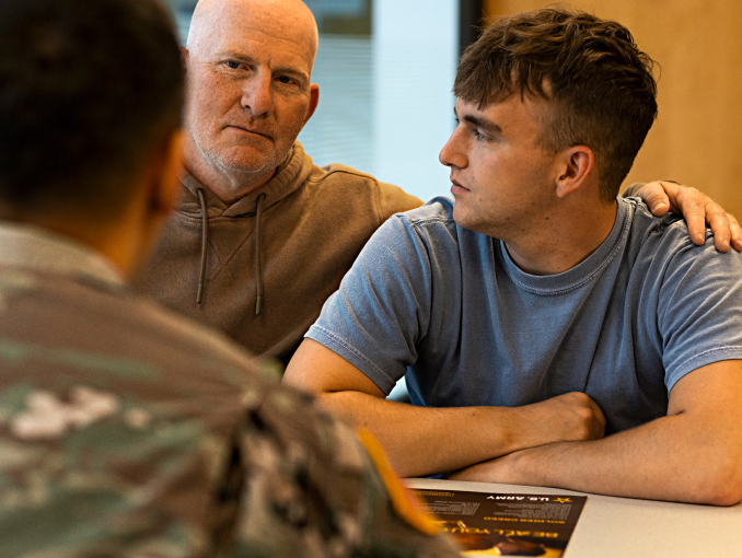 A father sitting next to his son at a desk across from an Army recruiter