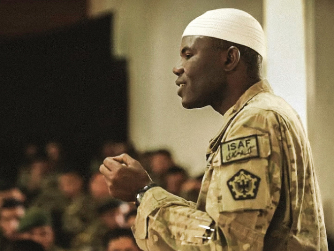 An Army Chaplain stands in front of seated Army members, all in uniform
