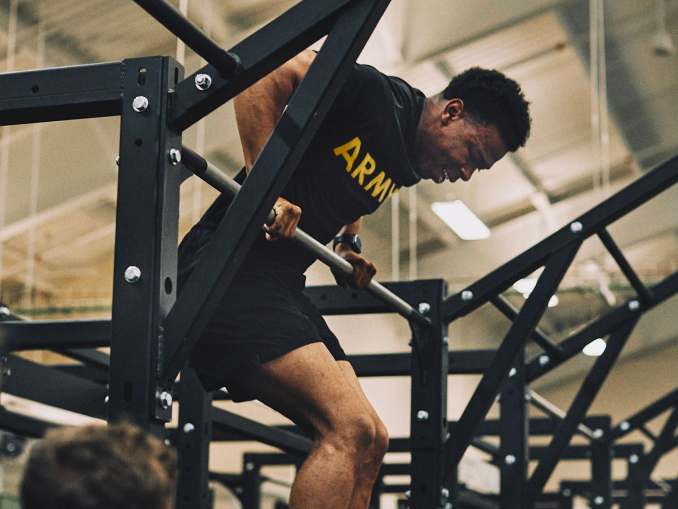 A male Soldier in an Army tee shirt performing a pull up bar pull over in a gym