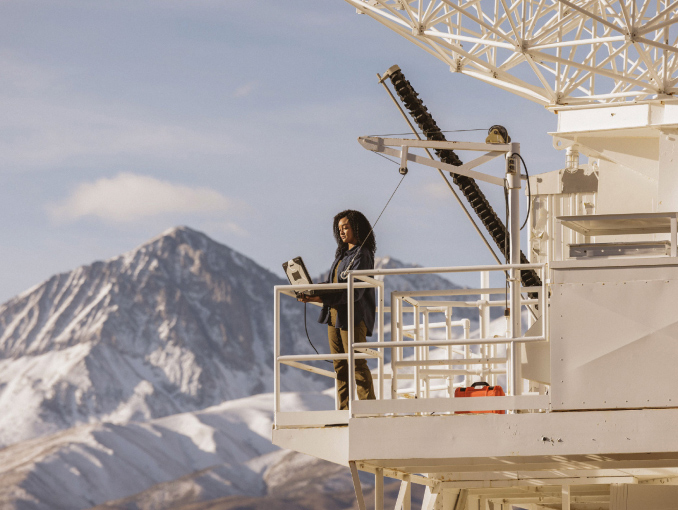 An Army Civilian satellite engineer standing on a satellite tower working on a laptop