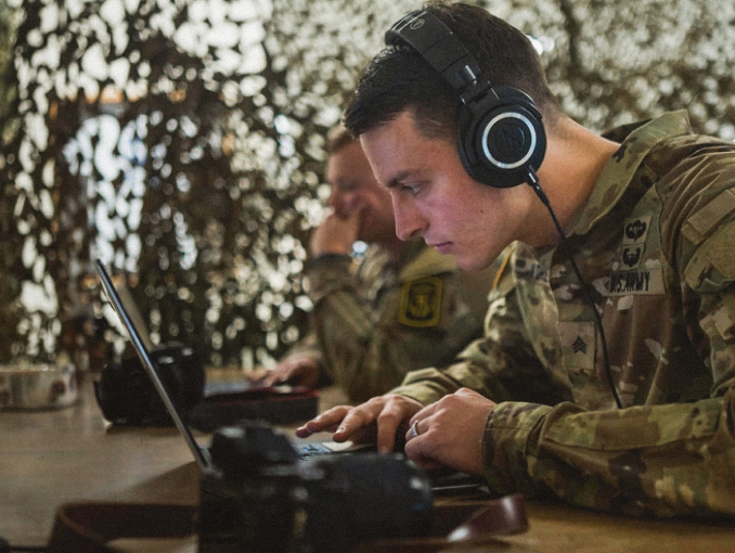 A Psychological Operations Soldier wearing headphones working on a laptop