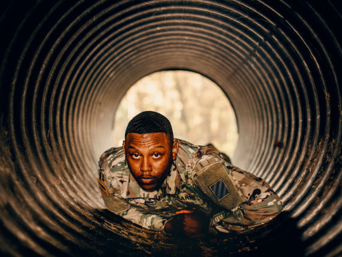 A male Soldier in combat uniform crawling through a tube