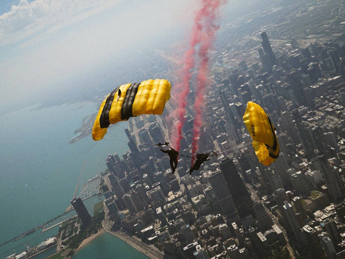 Two Golden Knights skydivers parachuting over a city