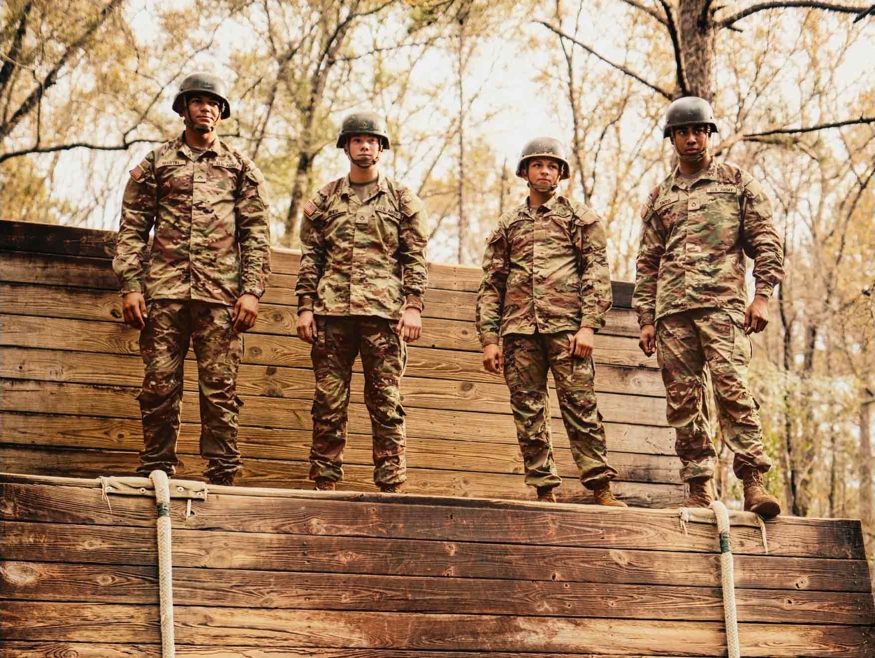 Cuatro Soldados en uniforme de combate parados en un obstáculo de madera al aire libre