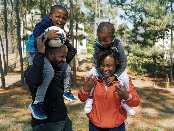 A smiling mother and father carrying their two sons over their shoulders