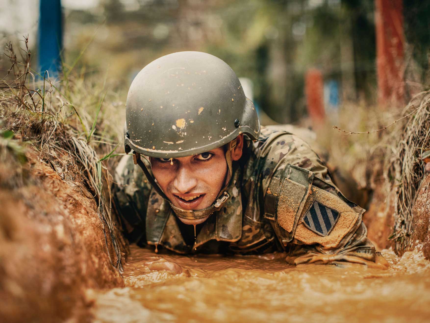 Un Soldado enlistado arrastrándose en el lodo durante un entrenamiento