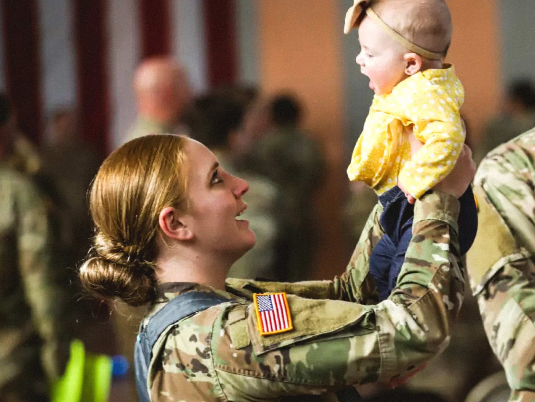 Female Soldier in combat uniform smiling and holding her baby in the air