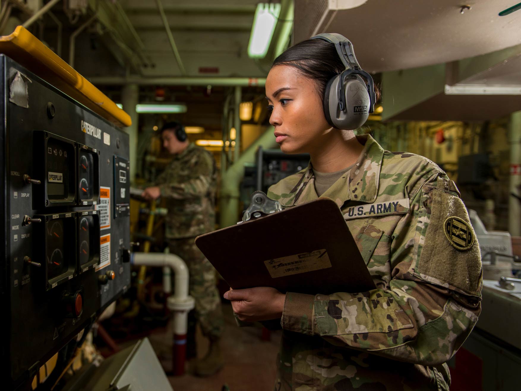 Una Soldado usando audífonos leyendo medidores en una embarcación del Army