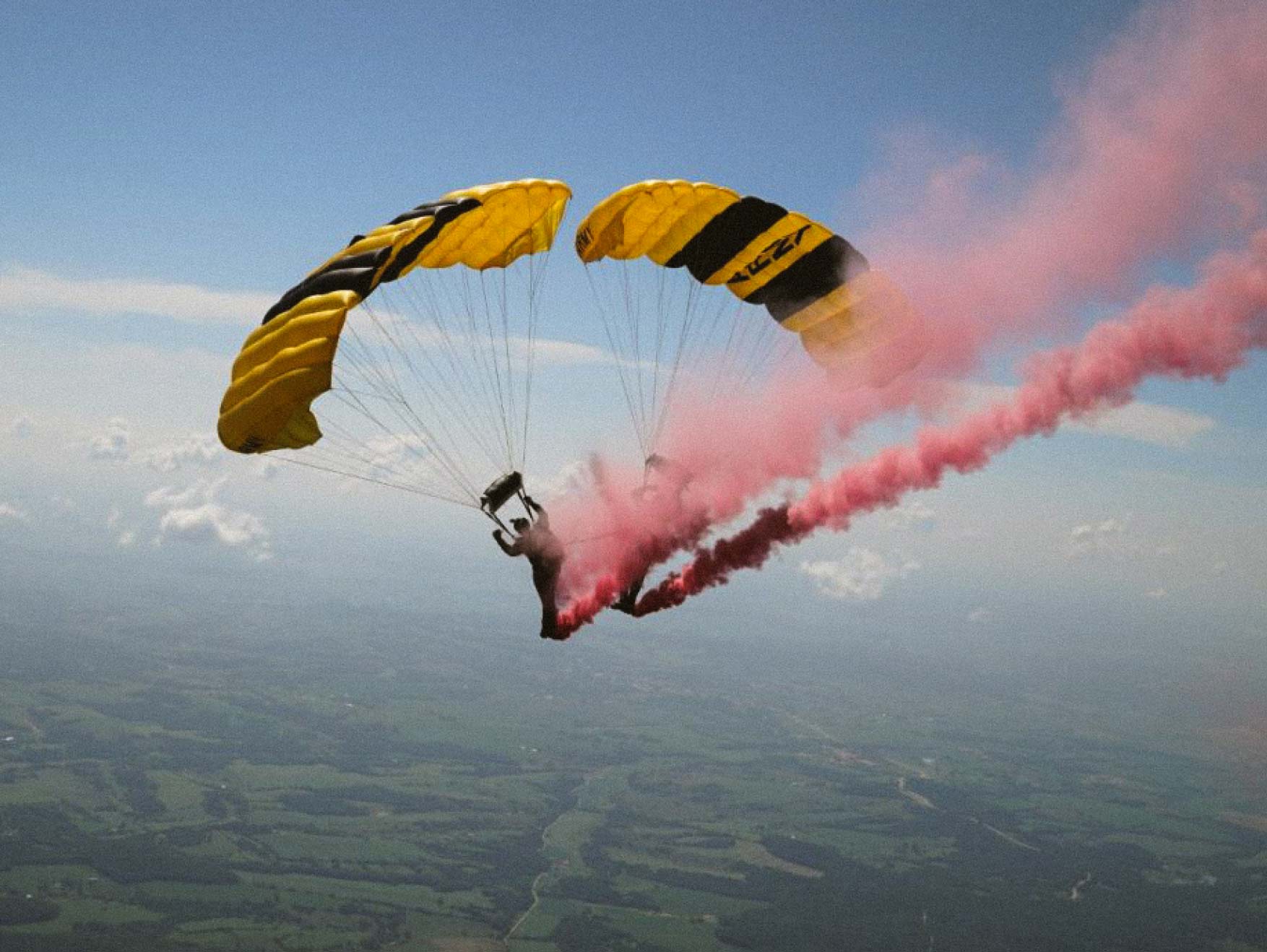 Two Golden Knights skydivers performing a jump leaving a trail of red smoke behind them