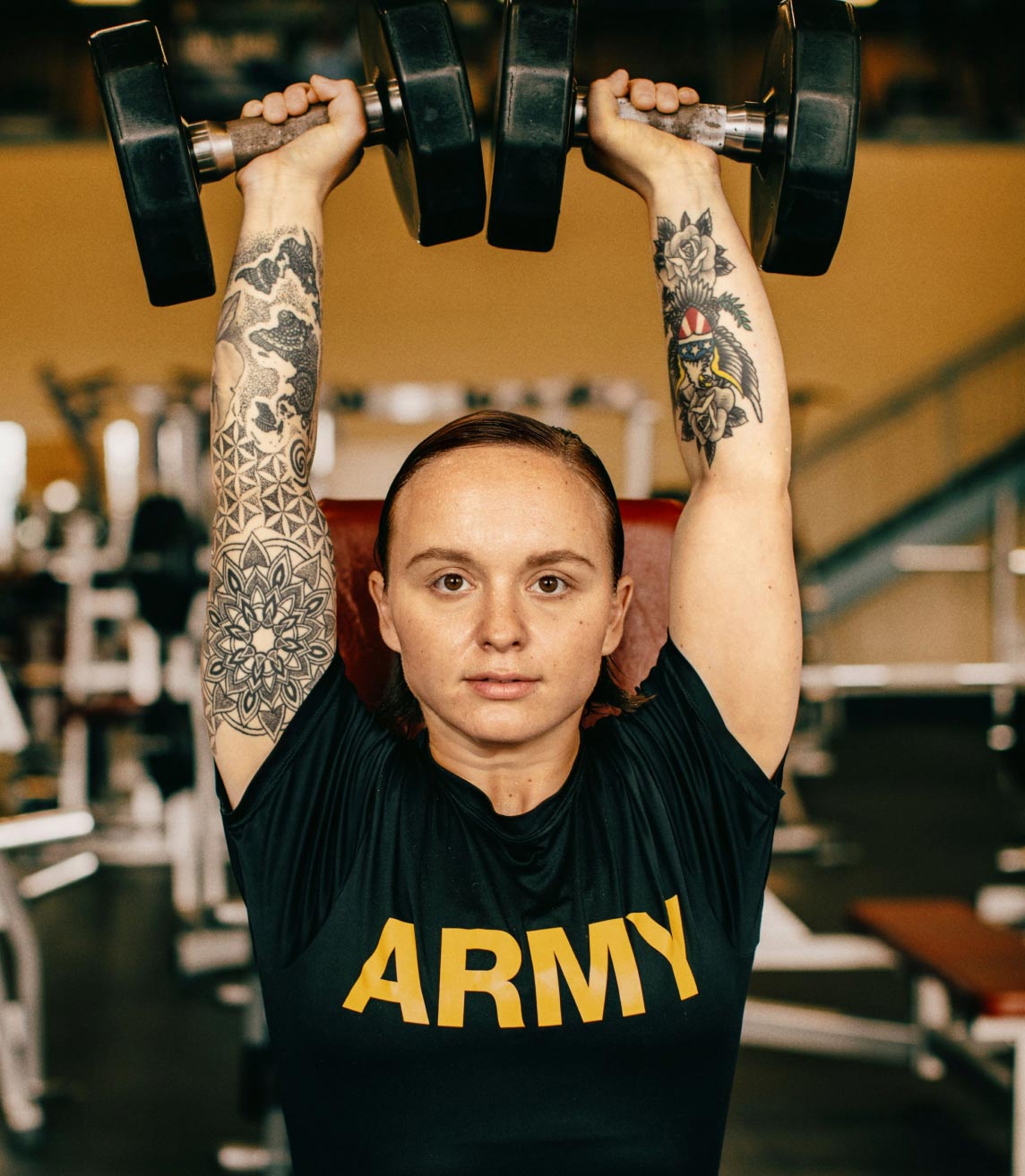 Female Soldier in an Army tee shirt lifting dumbells over her head