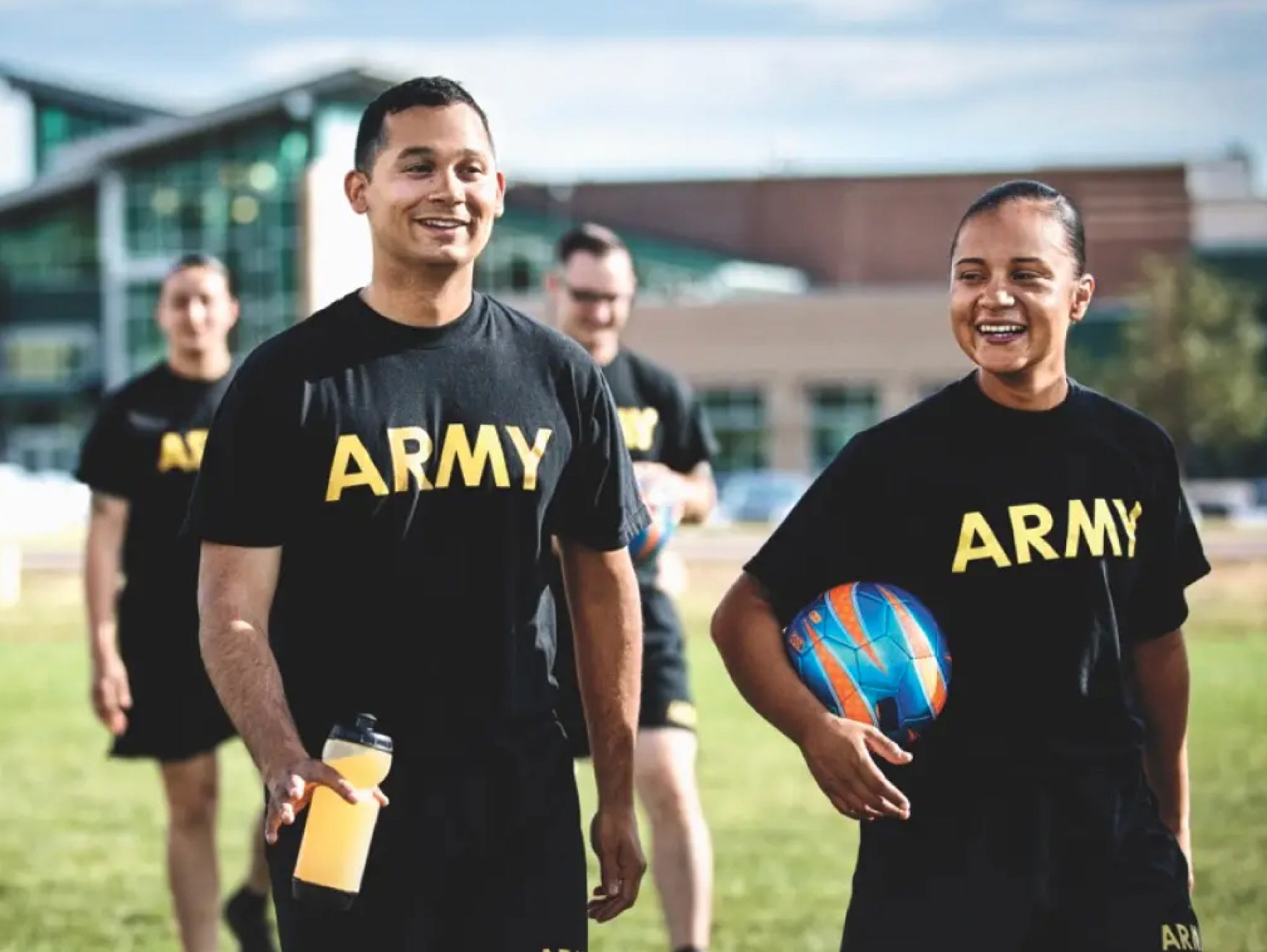 Three Soldiers in Army T-shirts, one holding a sports bottle and another holding a soccer ball