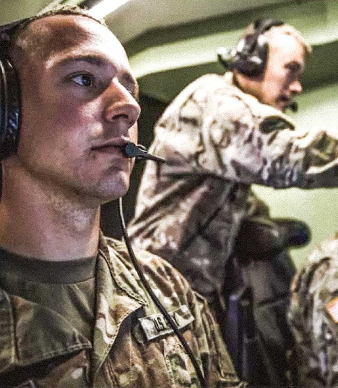 Tres Soldados del Army uniformados con audífonos mirando pantallas frente a ellos