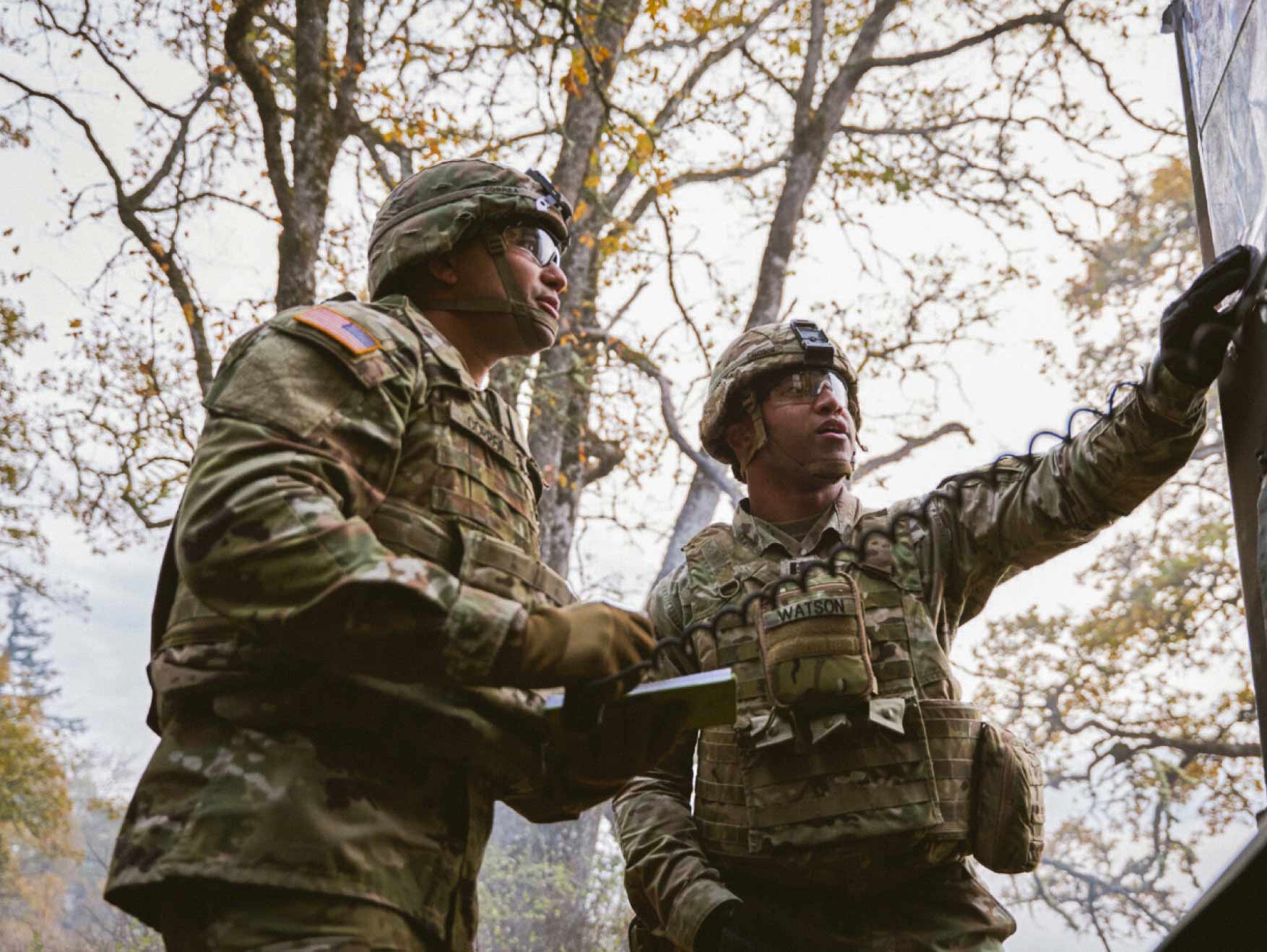 Two Soldiers in combat uniform looking at a bulletin board outside