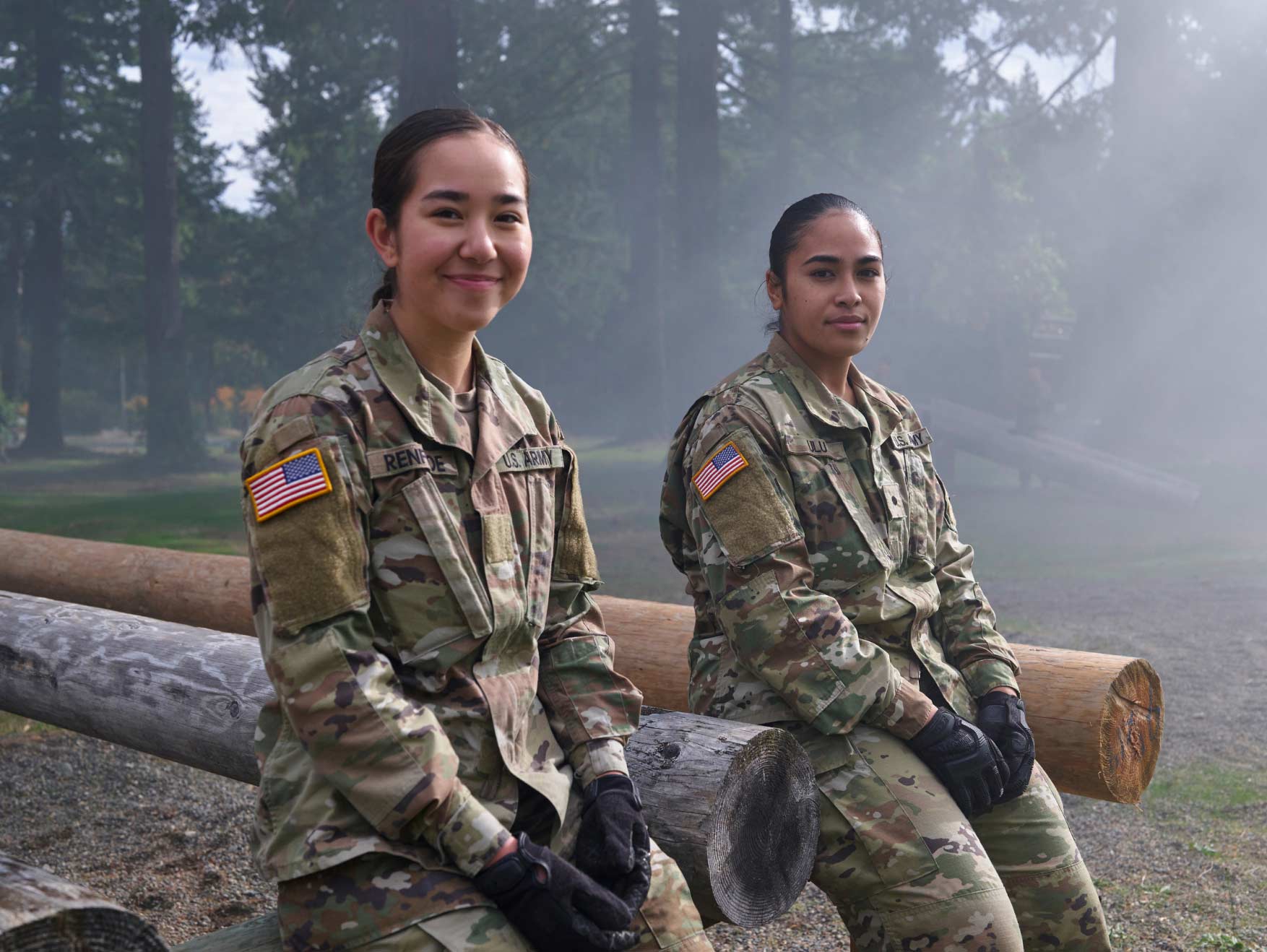 Two female ROTC cadets sitting outside against a wooden obstacle